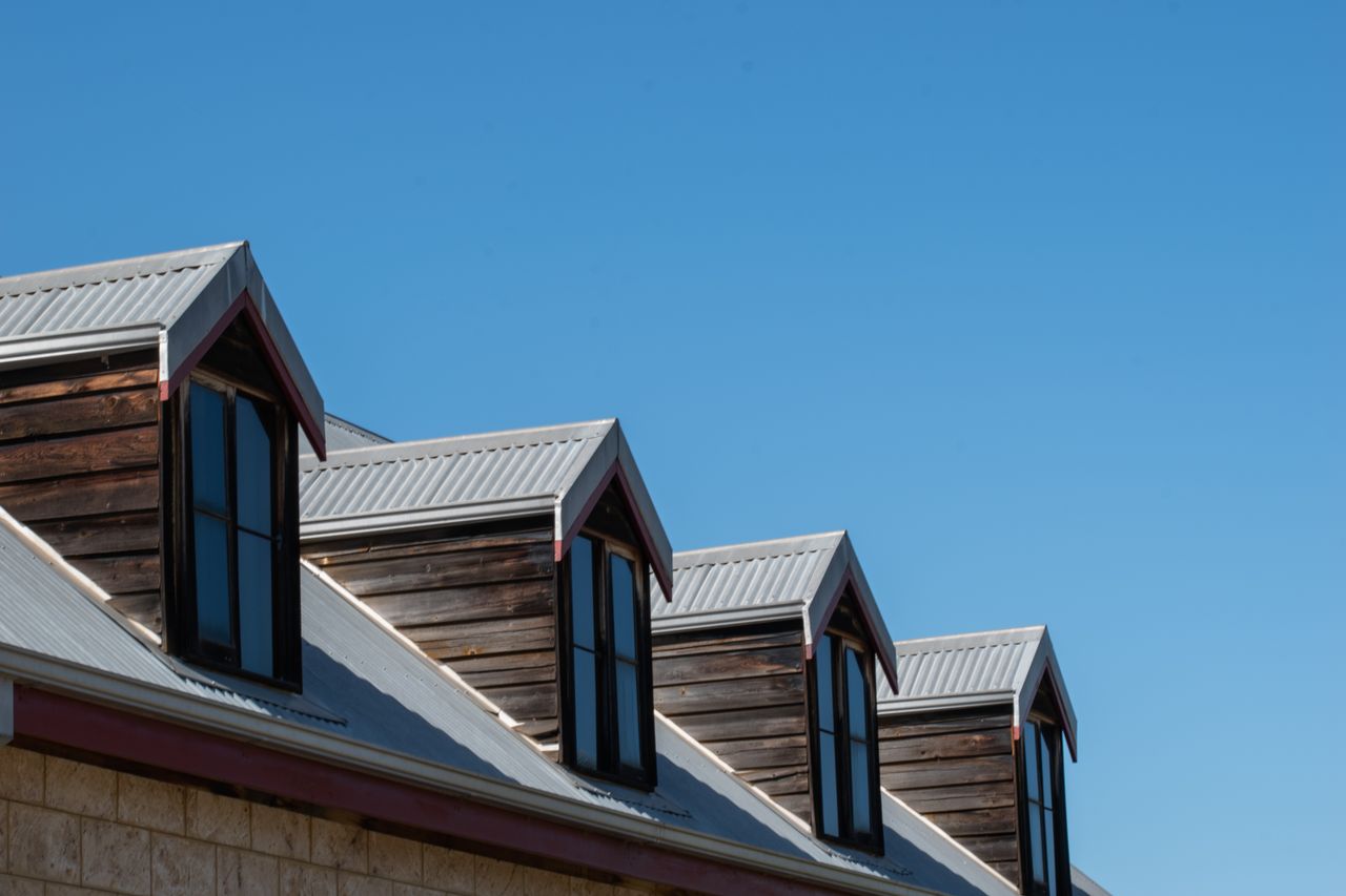 hero-img-01 Modern triangular rooftops with windows against a clear blue sky.