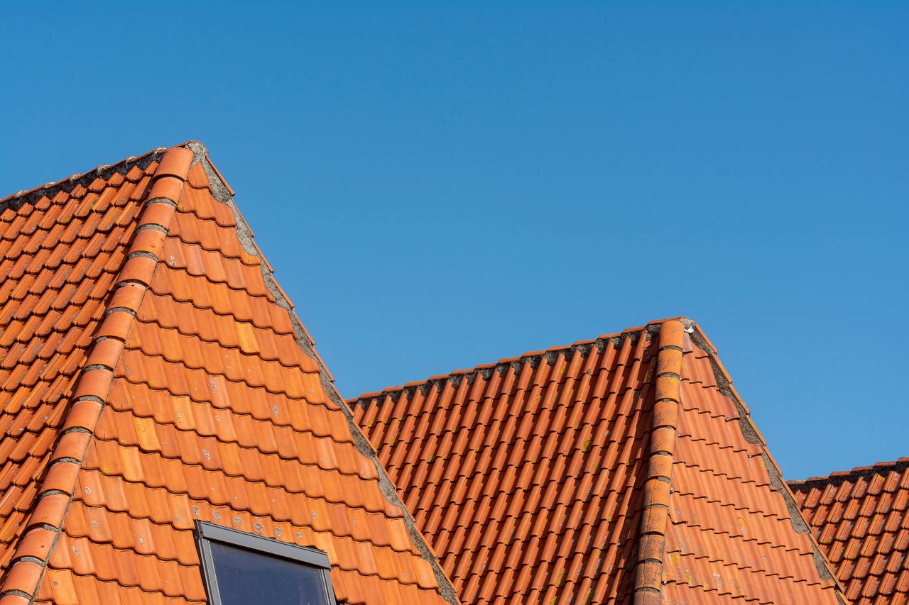 hero-img-02 Close-up of red tiled roofs under a clear blue sky, showcasing architectural design.