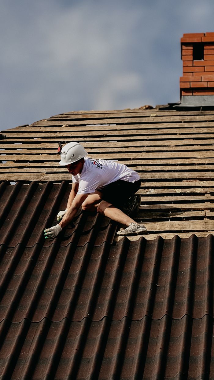services-03 A construction worker installs roofing tiles wearing protective gear on a sloped rooftop.