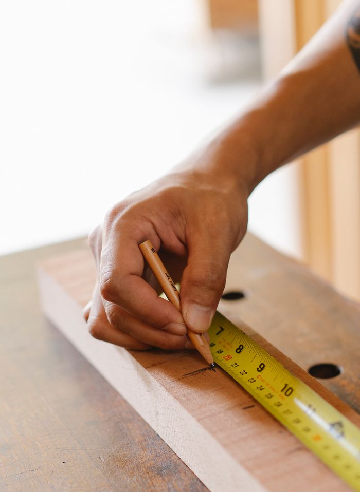 gallery-6 From above crop anonymous male joiner making sign with pencil measuring wooden plank while making handicraft in workshop