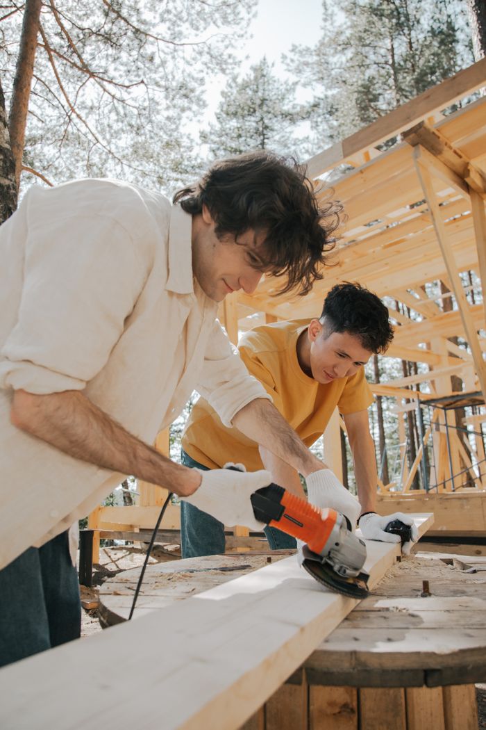 gallery-2 Two men working with power tools on an outdoor carpentry construction site.