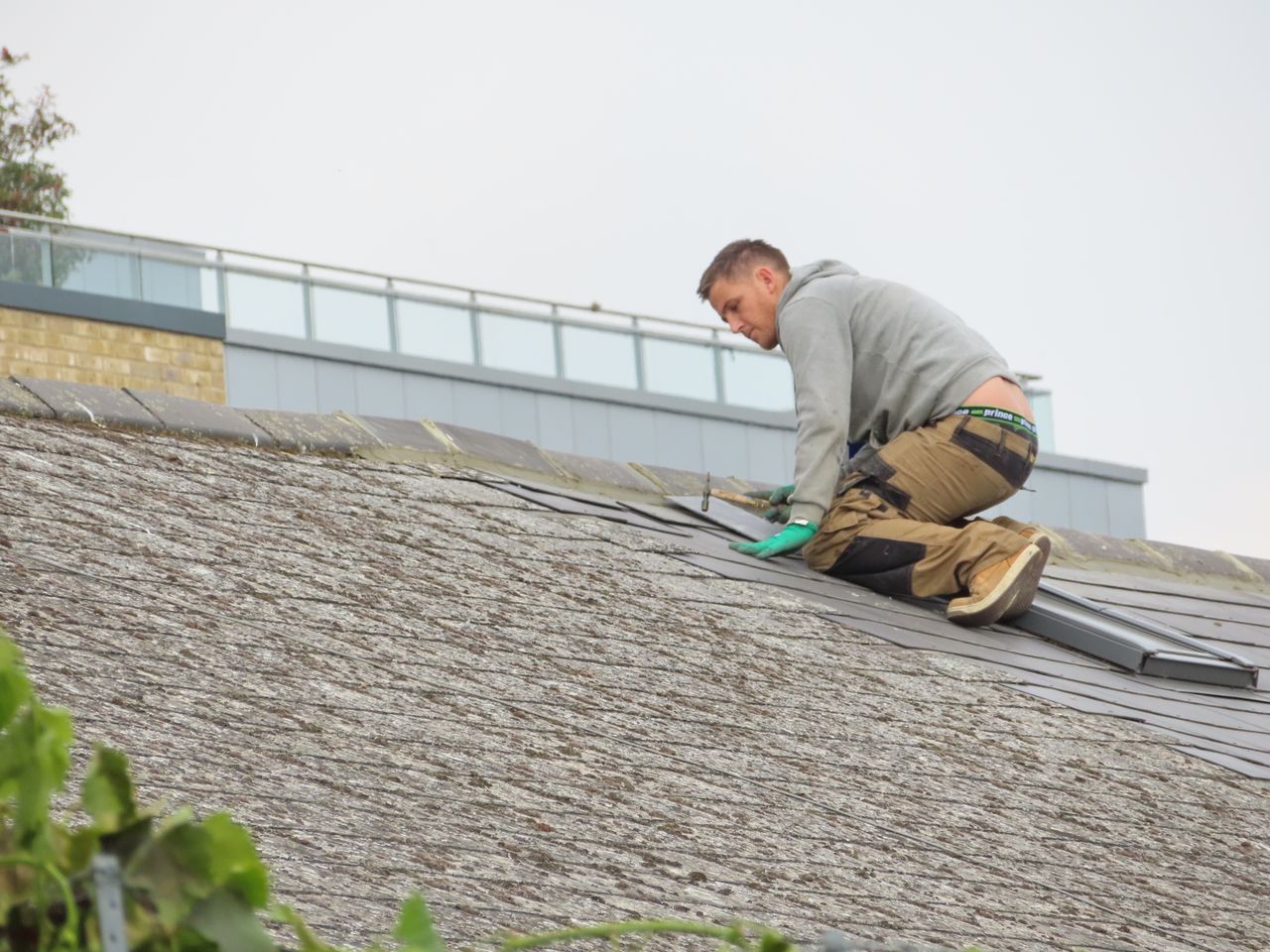 services-01 Construction worker installing shingles on a rooftop. Outdoor building maintenance.